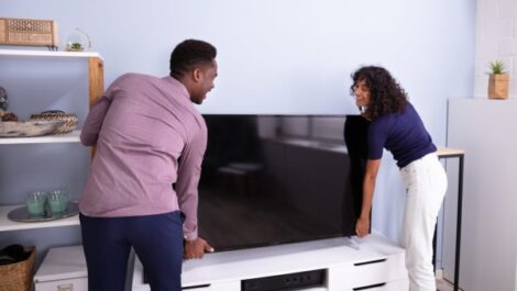 Two people lifting a TV in a room