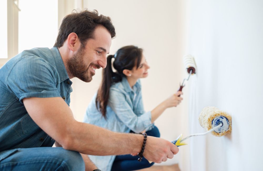 A man and woman happily painting a room to add value to their home.