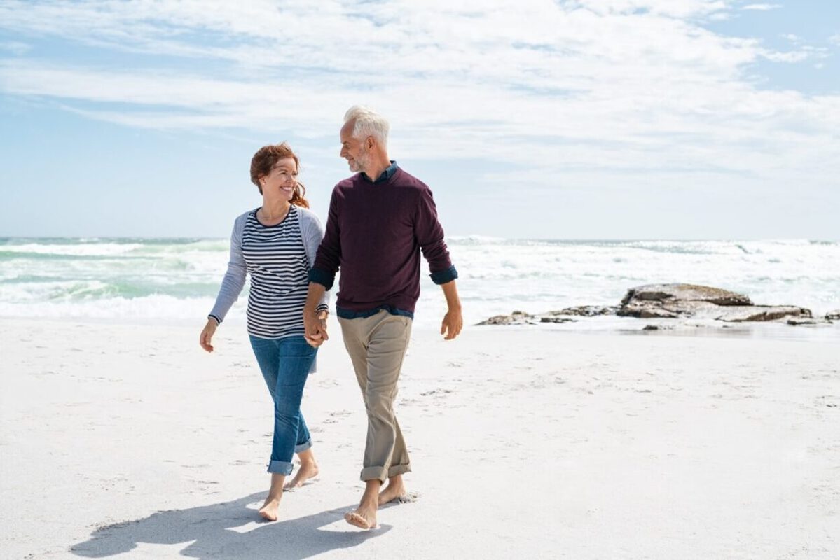 A senior couple walk on the beach for their retirement plan.