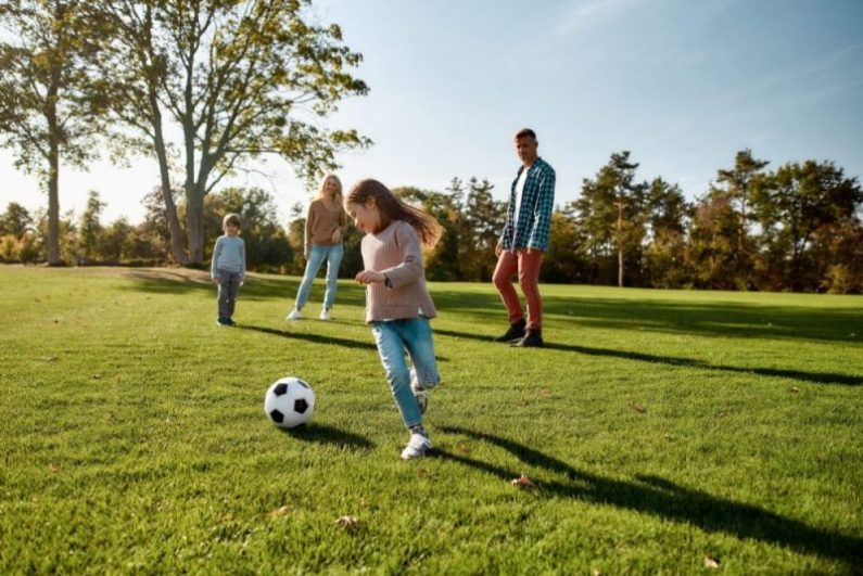 A family plays soccer outside in the summer.