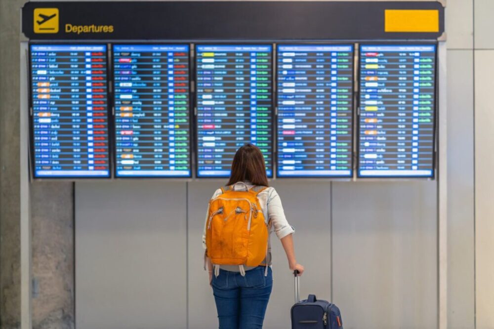 A young woman stands in front of the airport flight schedule.