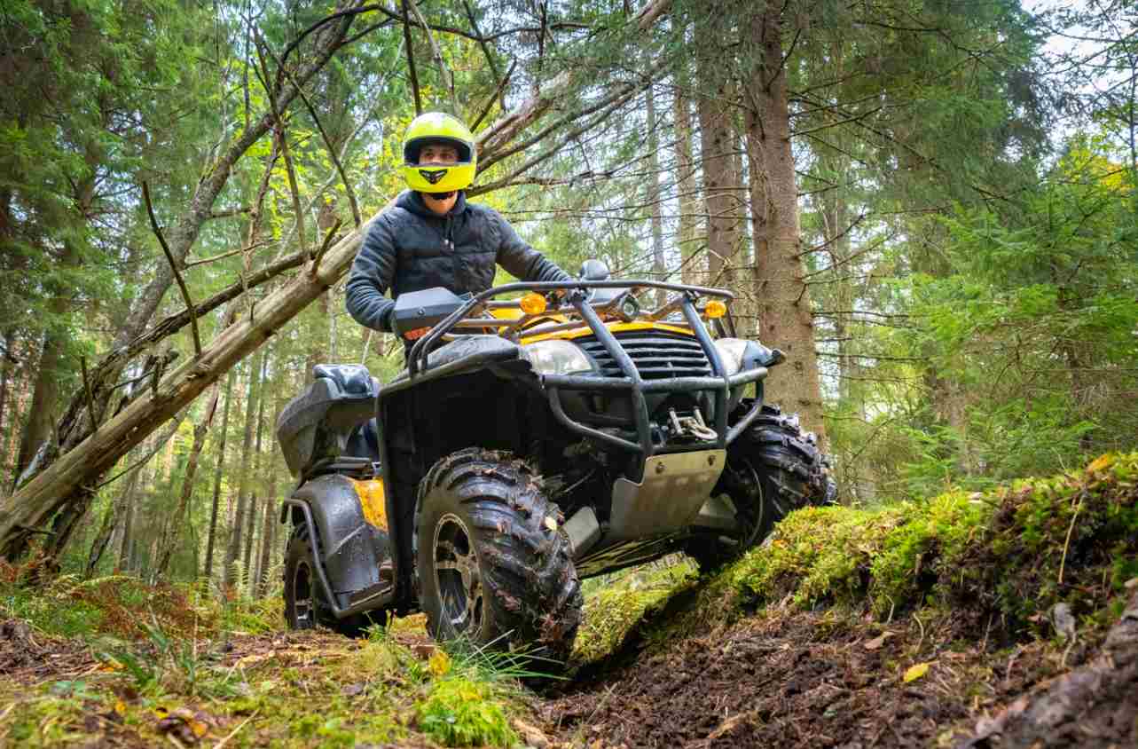Adult ATV driver wearing a jacket and helmet in the forest.