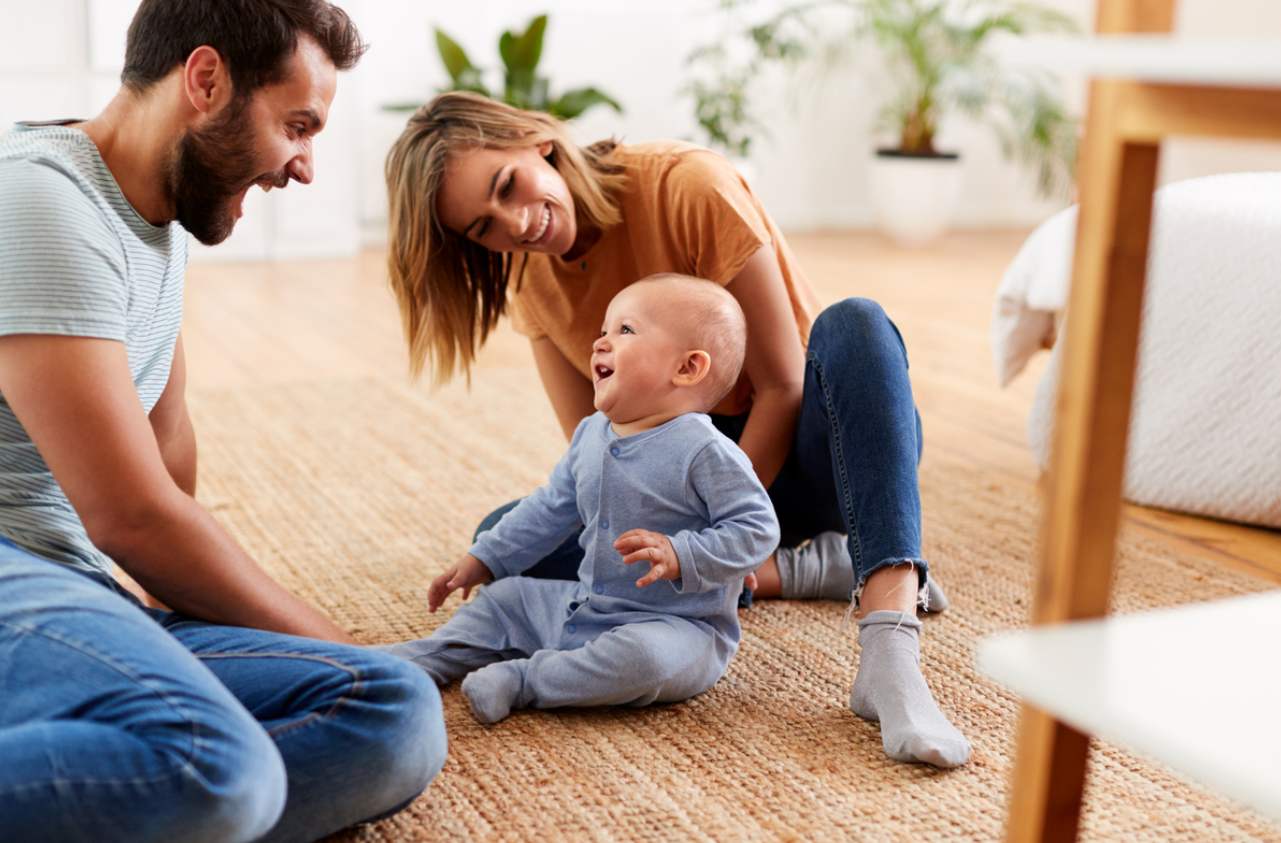 A family scene within a home living space including father, mother and child sitting on the floor laughing.