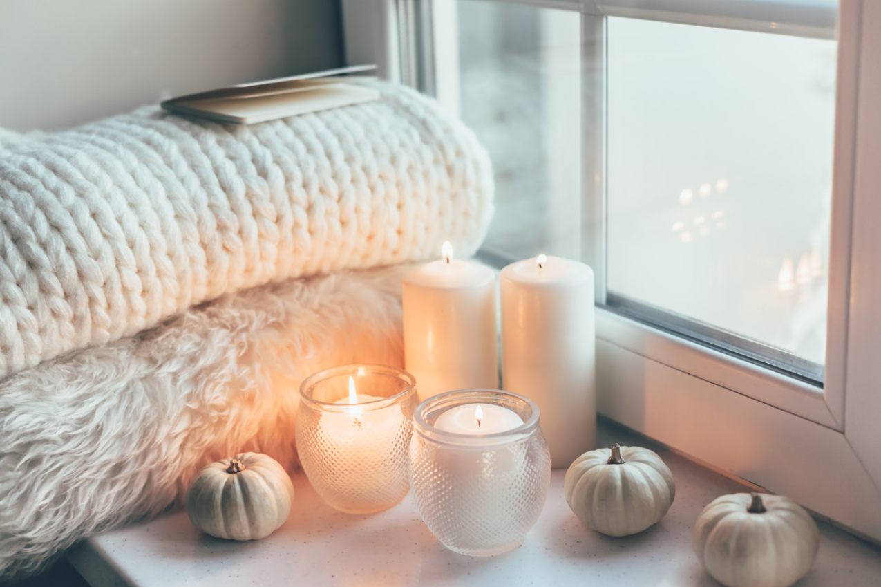 An arranged living space scene featuring lit candles and blankets against a window on a dreary day.