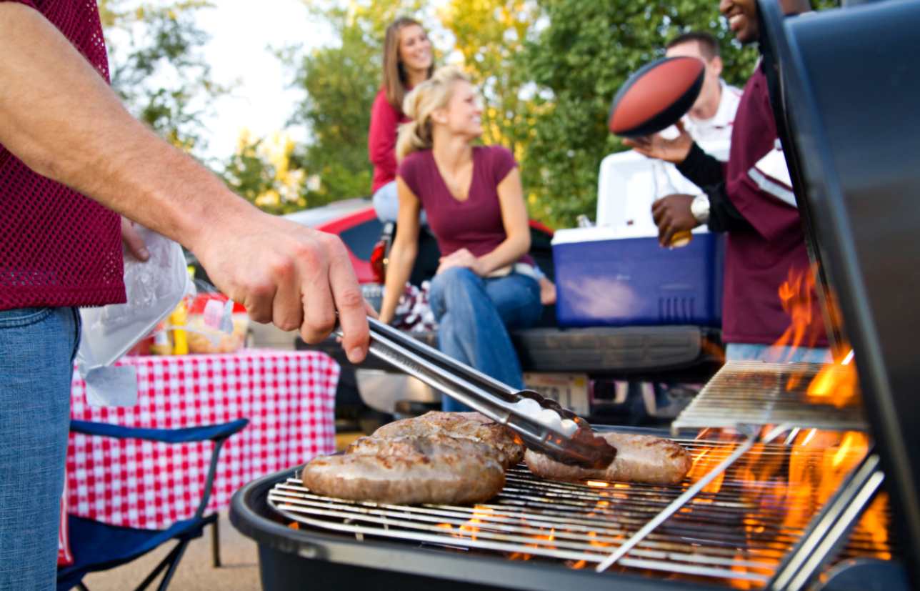 An ongoing outdoor BBQ scene with a manned grill and friends in the background talking.