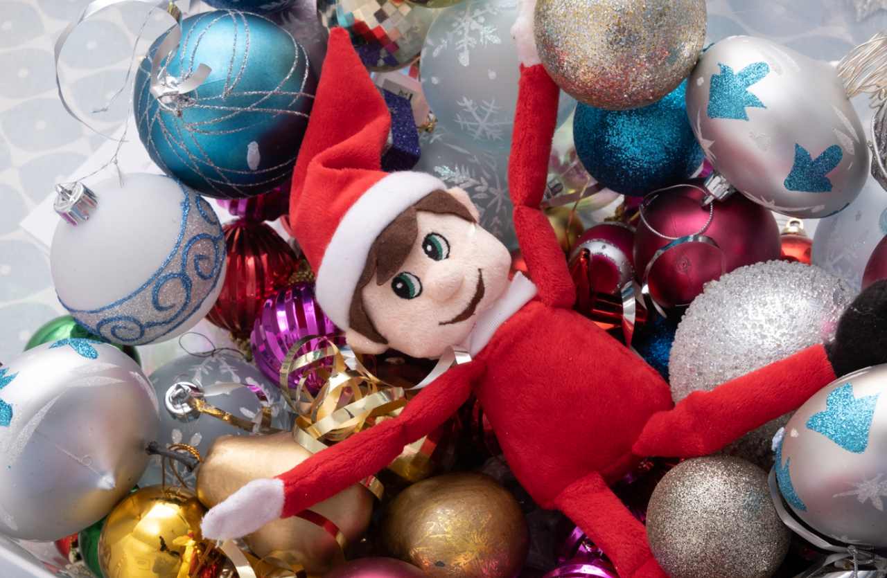 A Holiday-themed elf plush toy laying over a pile of Christmas tree ornaments.