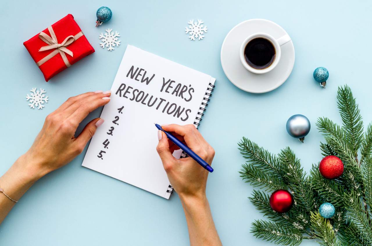 A person drafting a list of New Year's Resolutions in a notebook on a decorated tabletop.