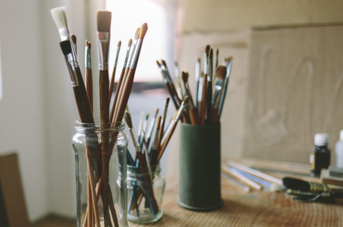 A close-up of paintbrushes and artists' supplies in clear glasses in a studio.
