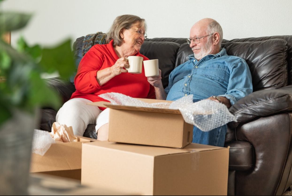 A photo of a couple sitting down for coffee amidst moving supplies.