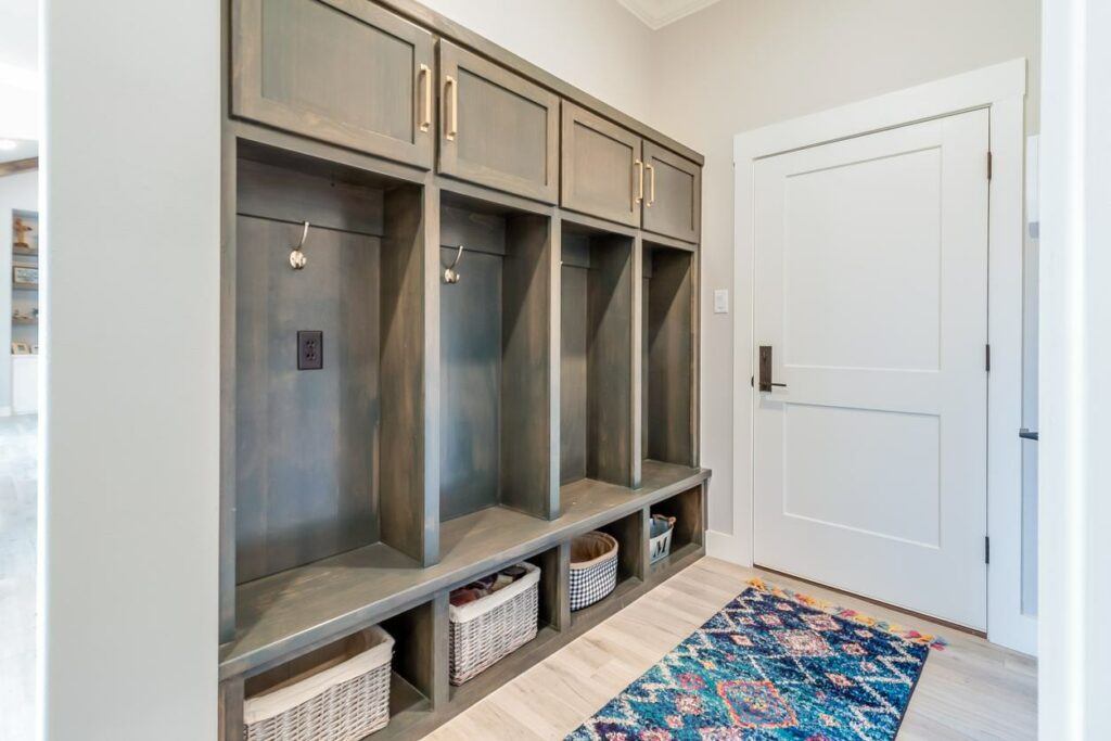 An organized mudroom with wooden cubbies and white wicker baskets with a blue and pink runner rug inside the door.