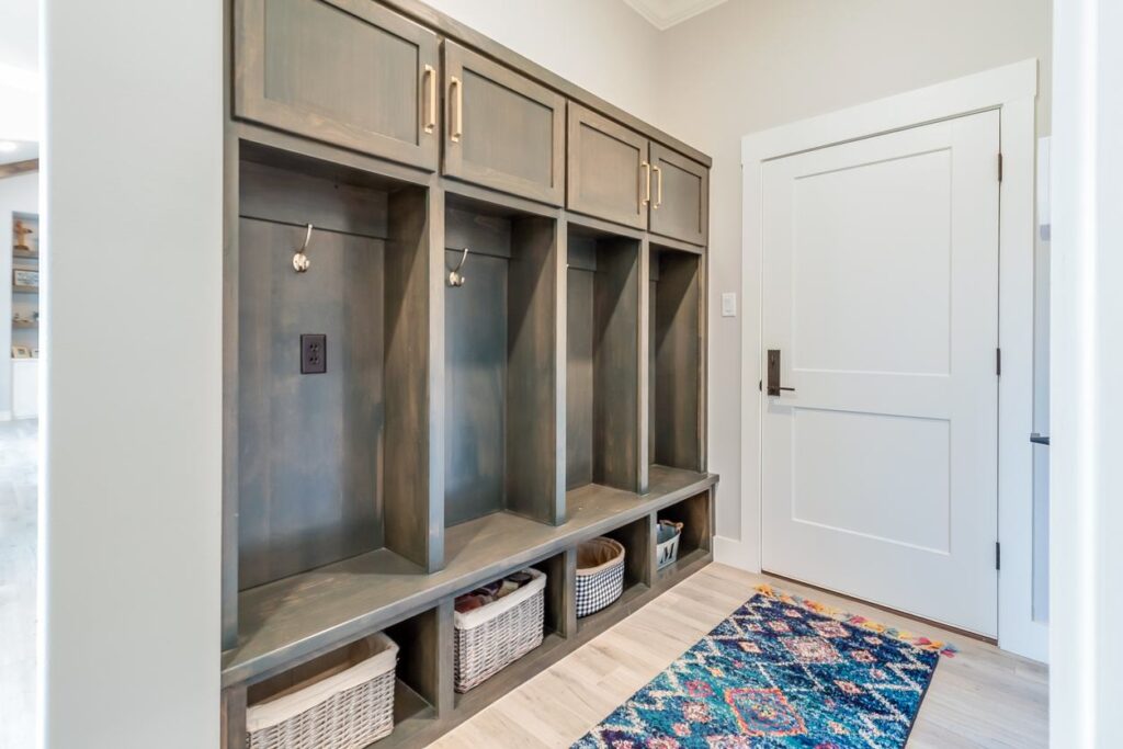 An organized mudroom with wooden cubbies and white wicker baskets with a blue and pink runner rug inside the door.