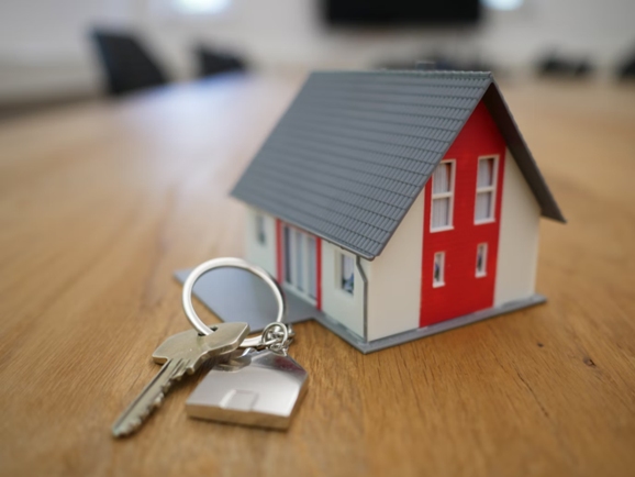 a set of keys sit by a miniature model house on a table