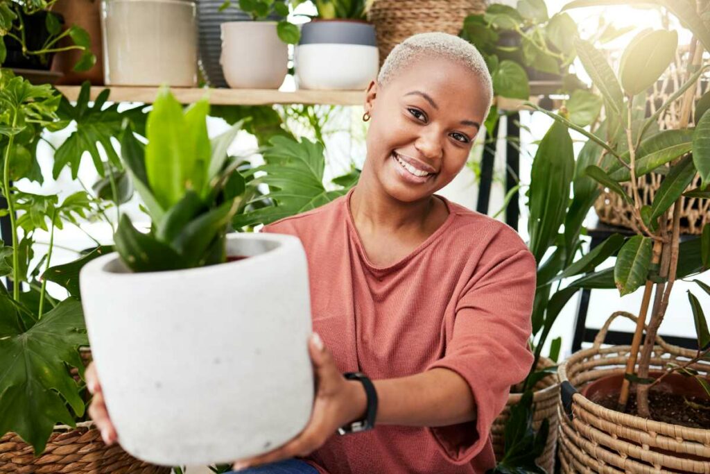 Portrait of a smiling woman holding a plant in a ceramic pot.