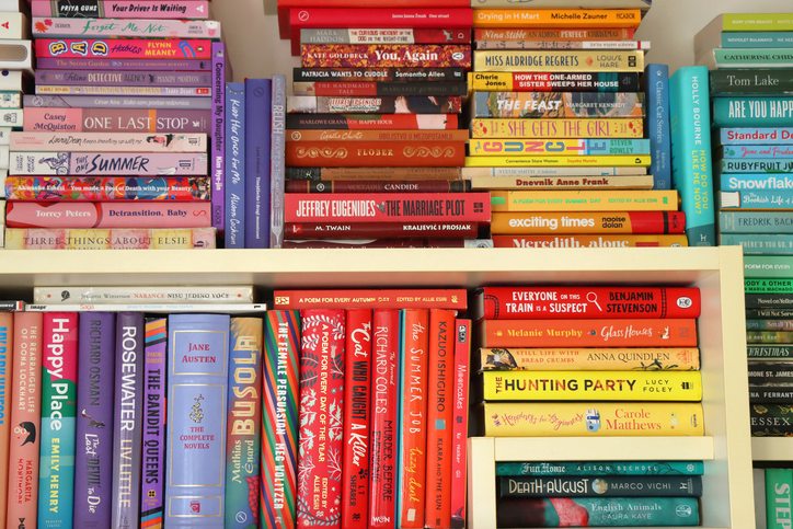 Stacks of books arranged by color on a cream bookshelf, creating a rainbow.