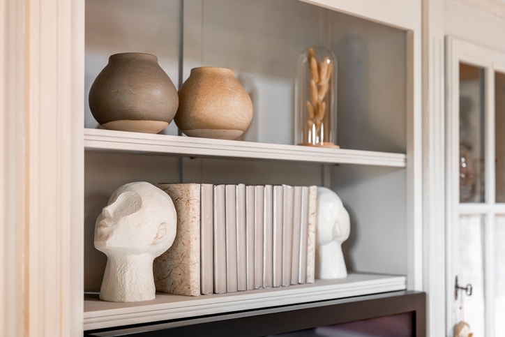 A minimalist-style bookshelf with head-shaped bookends, ceramic pots, and a vase.