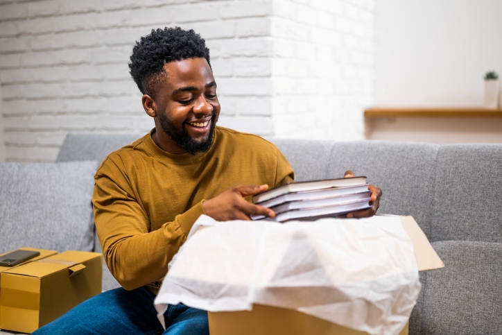 A smiling young man packs books into a box with paper.