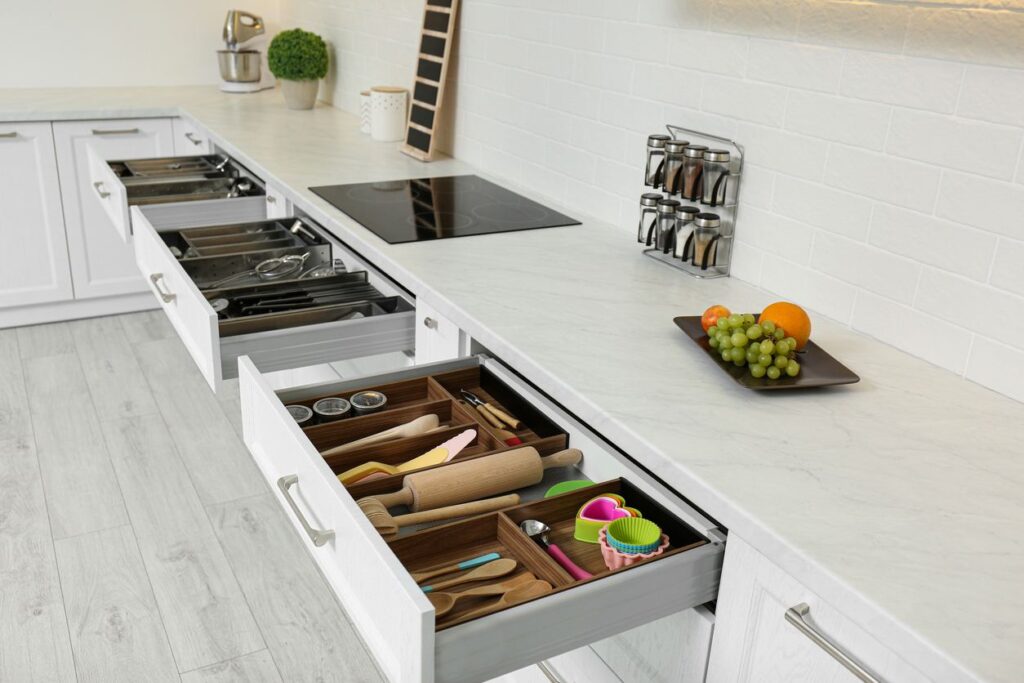 A row of open drawers that hold different and organized groups of kitchen utensils and cookware.